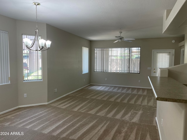 unfurnished dining area with dark colored carpet and ceiling fan with notable chandelier