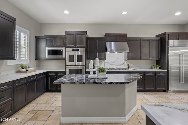 kitchen featuring a center island, dark stone counters, built in appliances, dark brown cabinetry, and extractor fan