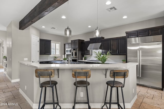 kitchen featuring beam ceiling, a large island with sink, appliances with stainless steel finishes, and a breakfast bar area