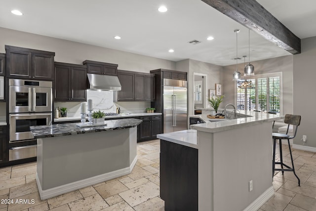 kitchen featuring dark stone counters, a spacious island, a breakfast bar area, decorative light fixtures, and stainless steel appliances