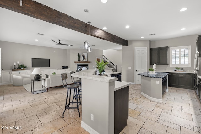 kitchen featuring a center island with sink, ceiling fan, beamed ceiling, decorative light fixtures, and a kitchen bar