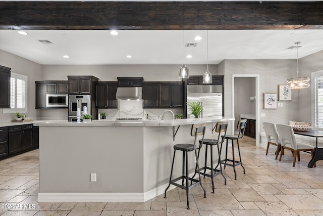 kitchen featuring a large island with sink, built in appliances, pendant lighting, and a breakfast bar area