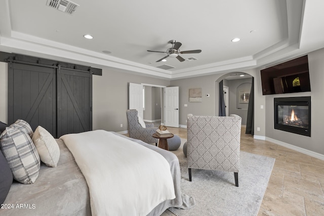 bedroom featuring a barn door, a tray ceiling, and ceiling fan