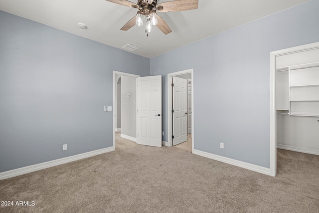 unfurnished bedroom featuring ceiling fan, a spacious closet, light carpet, and a closet