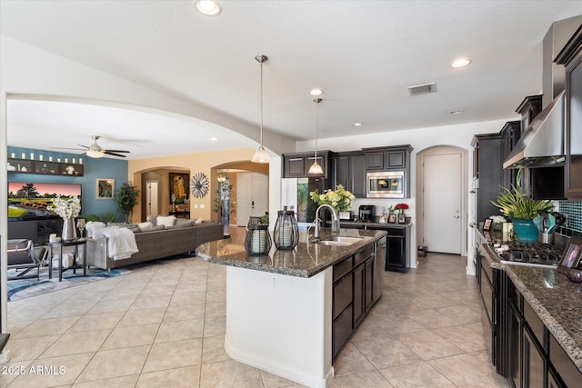 kitchen with dark brown cabinetry, sink, decorative light fixtures, a center island with sink, and stainless steel microwave