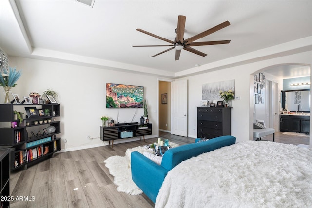 bedroom featuring connected bathroom, hardwood / wood-style floors, ceiling fan, and a tray ceiling