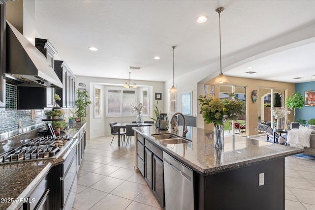 kitchen featuring sink, hanging light fixtures, stainless steel appliances, ventilation hood, and an island with sink