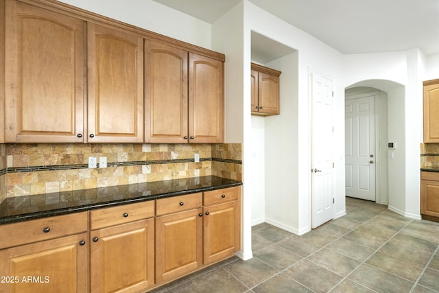 kitchen with dark stone counters, tasteful backsplash, brown cabinets, and baseboards