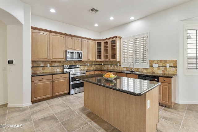 kitchen featuring a kitchen island, a sink, appliances with stainless steel finishes, dark stone counters, and glass insert cabinets