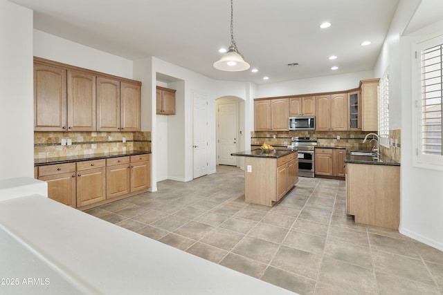 kitchen featuring arched walkways, a kitchen island, glass insert cabinets, stainless steel appliances, and a sink