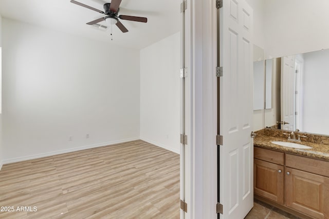 interior space featuring visible vents, a ceiling fan, a sink, light wood-type flooring, and baseboards