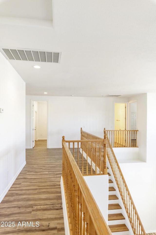 hall featuring baseboards, visible vents, wood finished floors, an upstairs landing, and recessed lighting