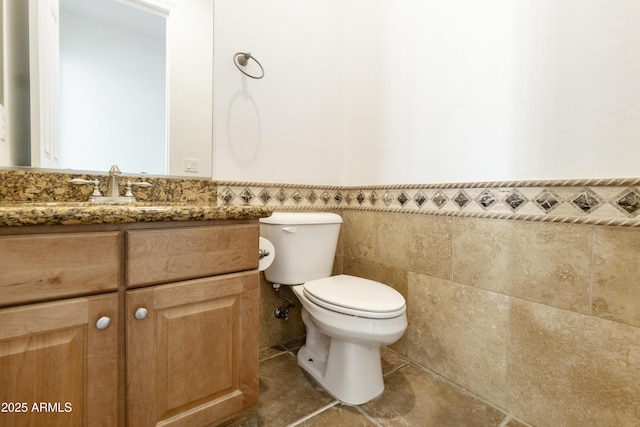 bathroom with wainscoting, toilet, tile patterned flooring, vanity, and tile walls