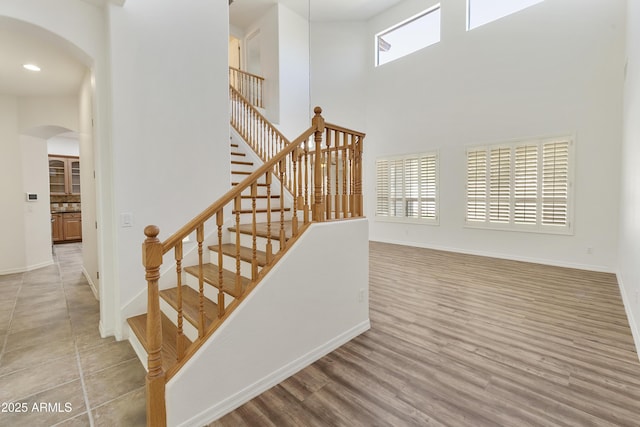 stairs featuring baseboards, a high ceiling, arched walkways, and wood finished floors