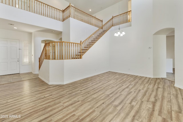 foyer with arched walkways, baseboards, light wood-style flooring, stairway, and an inviting chandelier