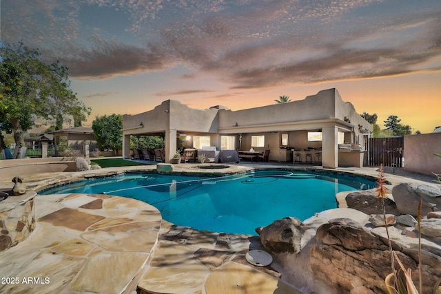 pool at dusk featuring a patio area, an outdoor kitchen, an outdoor pool, and fence