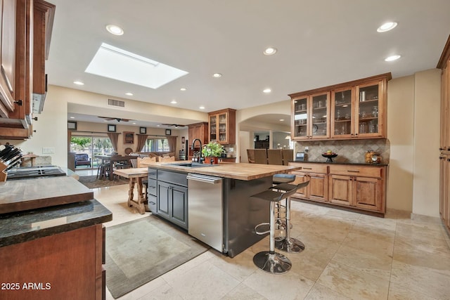 kitchen featuring wooden counters, open floor plan, a breakfast bar, arched walkways, and stainless steel dishwasher