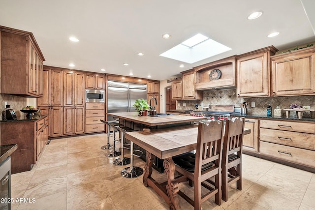 kitchen with decorative backsplash, built in appliances, dark countertops, and a skylight