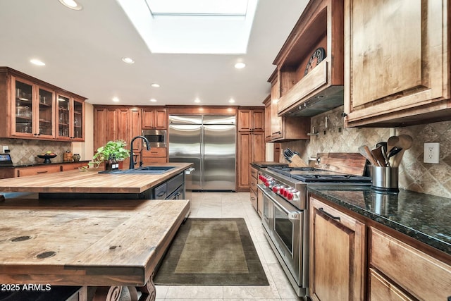 kitchen featuring brown cabinets, a sink, a skylight, butcher block counters, and built in appliances