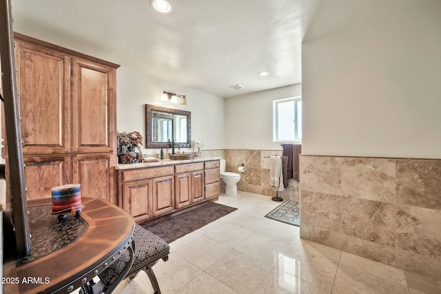 full bath with tile patterned floors, toilet, tile walls, wainscoting, and vanity