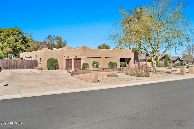 pueblo revival-style home with concrete driveway, fence, a garage, and stucco siding