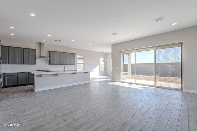 kitchen featuring a center island with sink, light hardwood / wood-style flooring, wall chimney exhaust hood, decorative backsplash, and a breakfast bar area