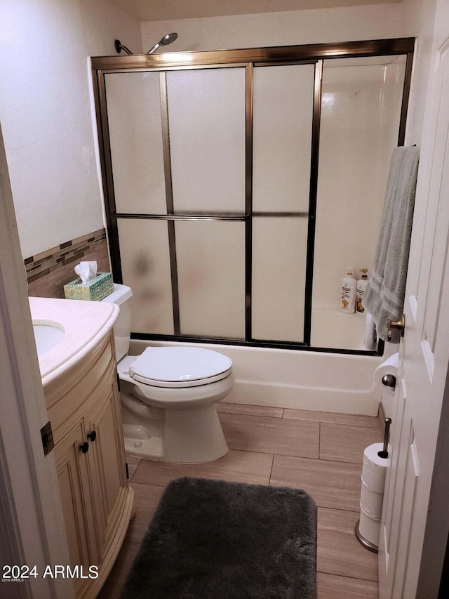 full bathroom with shower / bath combination with glass door, vanity, toilet, and tile walls