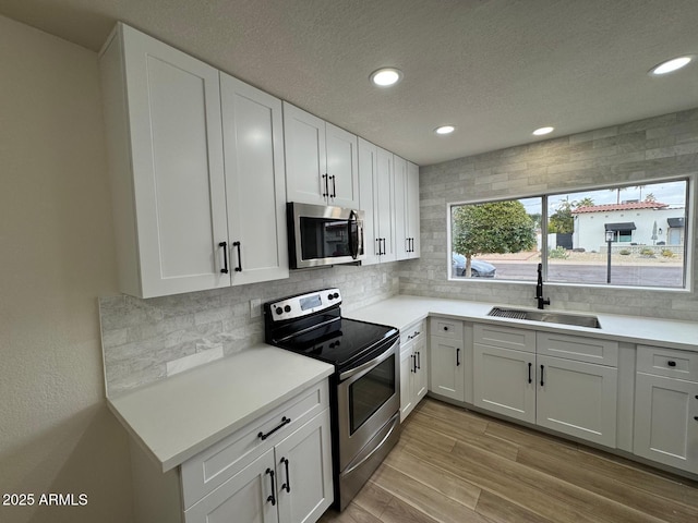 kitchen featuring appliances with stainless steel finishes, white cabinetry, sink, decorative backsplash, and light wood-type flooring