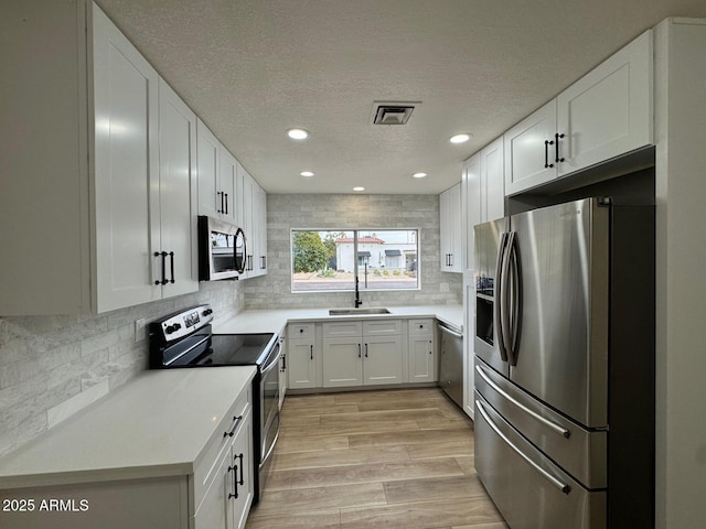 kitchen featuring tasteful backsplash, white cabinetry, sink, stainless steel appliances, and light hardwood / wood-style flooring