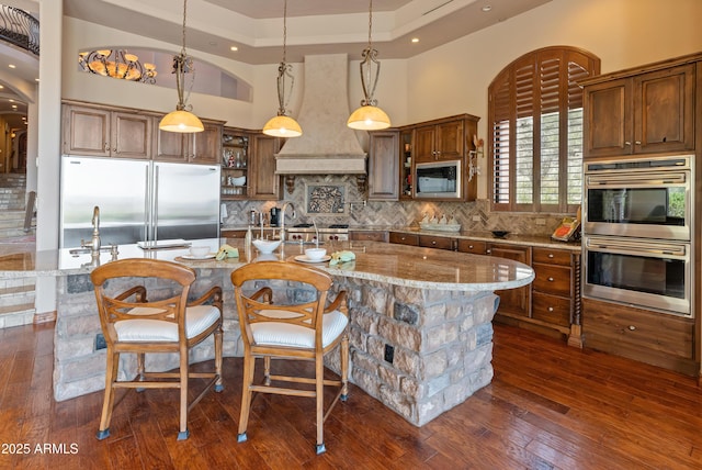 11550 E Paradise Ln, Scottsdale, AZ 85255 - kitchen featuring built in appliances, decorative backsplash, custom range hood, light stone counters, and decorative light fixtures