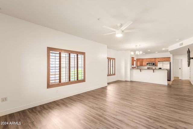 unfurnished living room with wood-type flooring and ceiling fan with notable chandelier