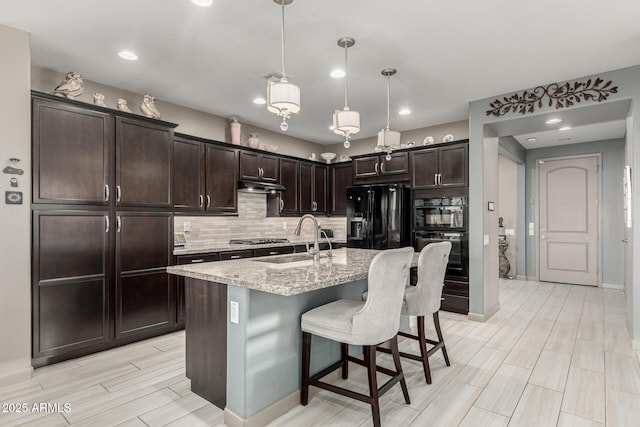 20784 W Minnezona Ave, Buckeye, AZ 85396 - kitchen with a sink, black appliances, under cabinet range hood, light stone countertops, and dark brown cabinetry