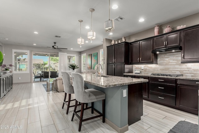 20784 W Minnezona Ave, Buckeye, AZ 85396 - kitchen featuring a sink, under cabinet range hood, tasteful backsplash, light stone counters, and recessed lighting