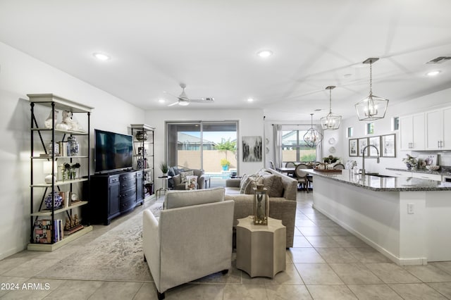 tiled living room featuring ceiling fan with notable chandelier and sink