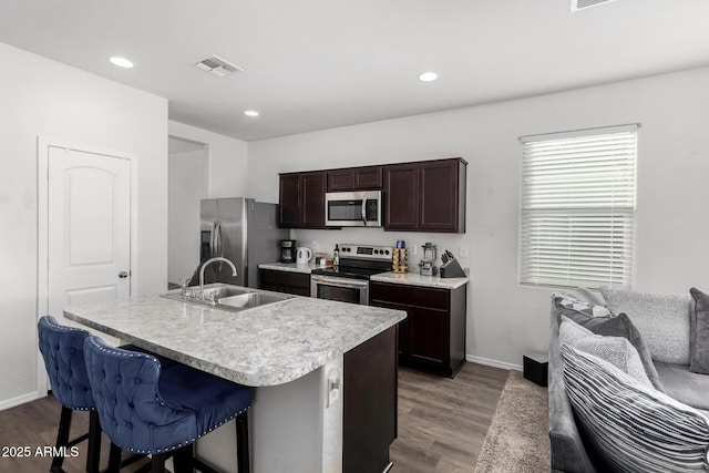 kitchen featuring stainless steel appliances, a sink, visible vents, a kitchen breakfast bar, and dark wood-style floors