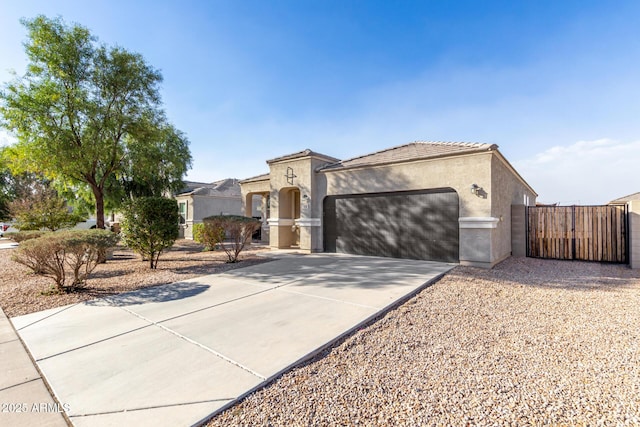 mediterranean / spanish-style home with an attached garage, concrete driveway, a tiled roof, a gate, and stucco siding