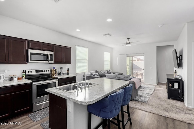 kitchen featuring stainless steel appliances, light countertops, open floor plan, a sink, and an island with sink