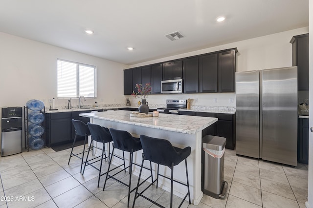 kitchen with a center island, a kitchen bar, sink, stainless steel appliances, and light stone counters