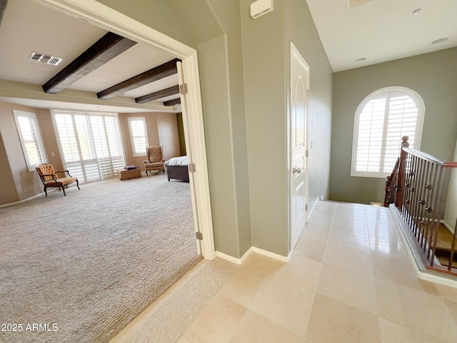 hallway with baseboards, visible vents, beamed ceiling, and light colored carpet