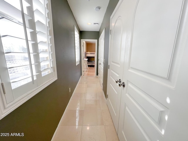 hall featuring light tile patterned floors, visible vents, and baseboards