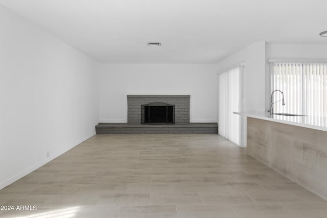 unfurnished living room with light hardwood / wood-style floors, sink, and a fireplace