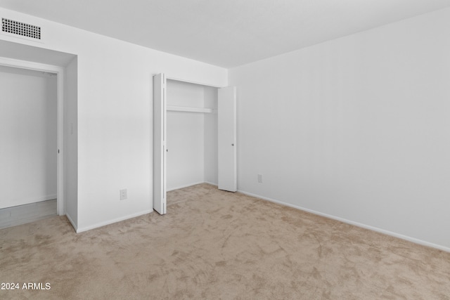 unfurnished bedroom with light colored carpet and a closet