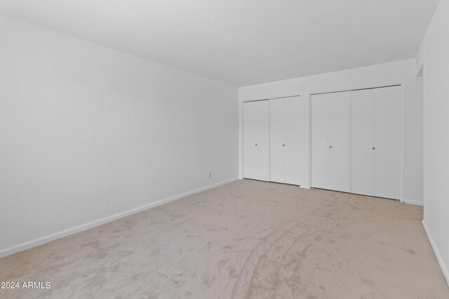 unfurnished bedroom featuring light carpet and multiple closets