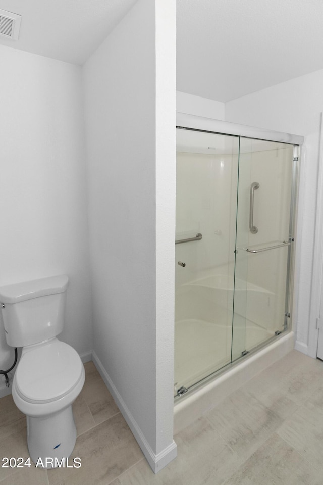 bathroom with a shower with shower door, tile patterned floors, and toilet