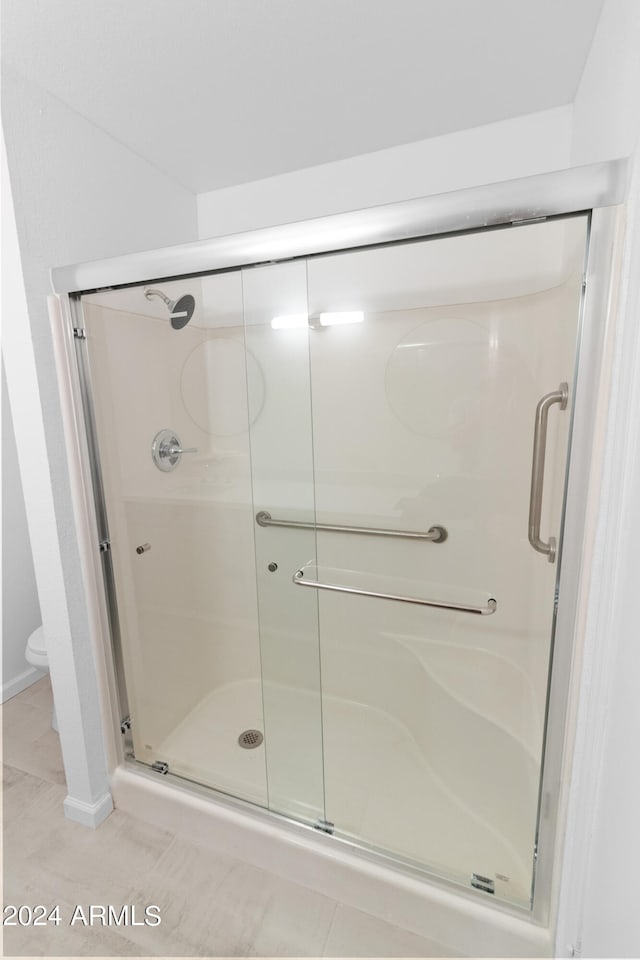 bathroom featuring a shower with shower door, tile patterned flooring, and toilet