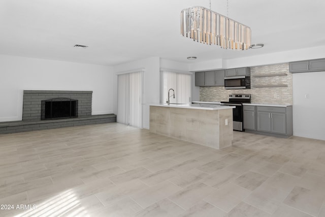 kitchen with gray cabinets, tasteful backsplash, an island with sink, appliances with stainless steel finishes, and a brick fireplace