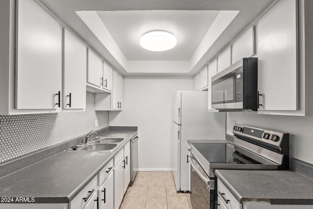 kitchen with white cabinets, sink, appliances with stainless steel finishes, a tray ceiling, and light tile patterned flooring