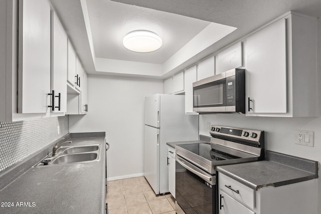 kitchen featuring sink, light tile patterned floors, a raised ceiling, white cabinets, and appliances with stainless steel finishes