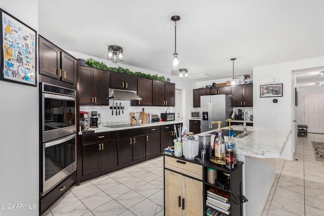 kitchen with decorative backsplash, dark brown cabinets, stainless steel appliances, and an island with sink