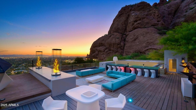 pool at dusk featuring a deck and an outdoor living space with a fire pit